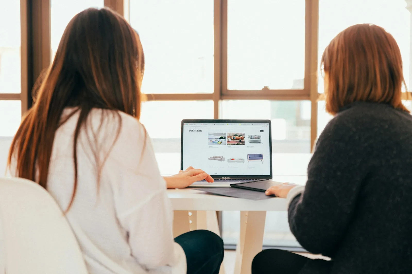 Two women working at a laptop by a window
